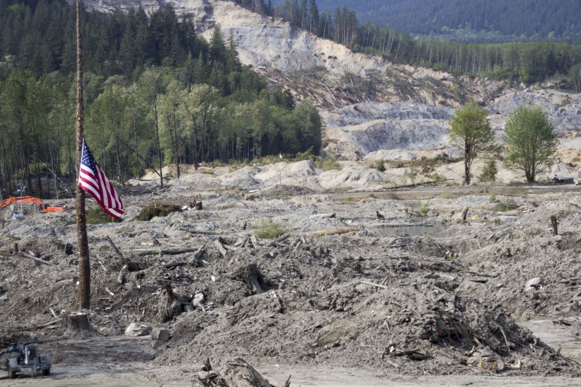 An+American+flag+lowered+to+half-mast+in+front+of+the+site+of+the+Highway+530+mudslide.