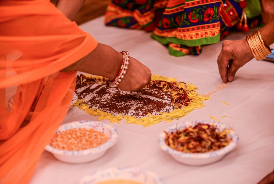 Several women create a Rangoli made of flower petals and seeds on the floor on Saturday night at Pullman Ashram.