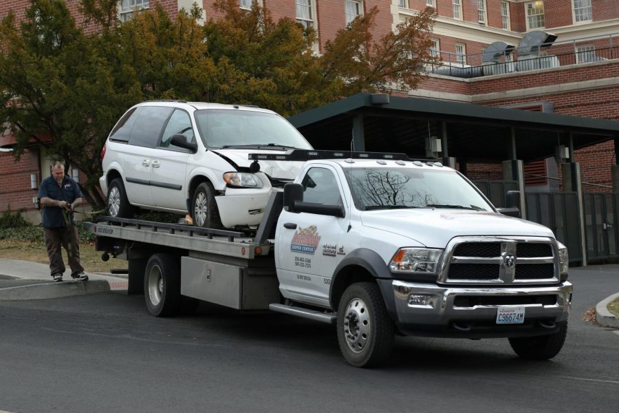 A white Chrysler Town & Country minivan was loaded onto the flatbed of a tow truck on Friday afternoon near the back entrance to Hillside Cafe. Bobby Graham, Auto Body Super Center tow truck driver, attaches tow straps through the rims of the minivan to hold it in place.