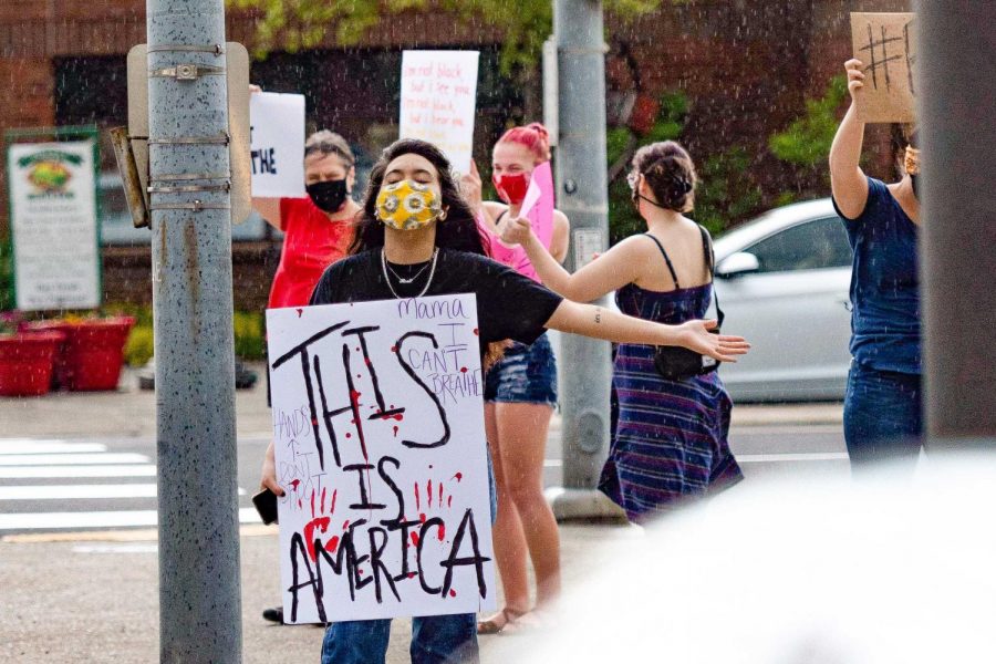Pullman resident and high school student Rose Maria Robles raises her arms to feel the rain hit her face while holding a This Is America sign.