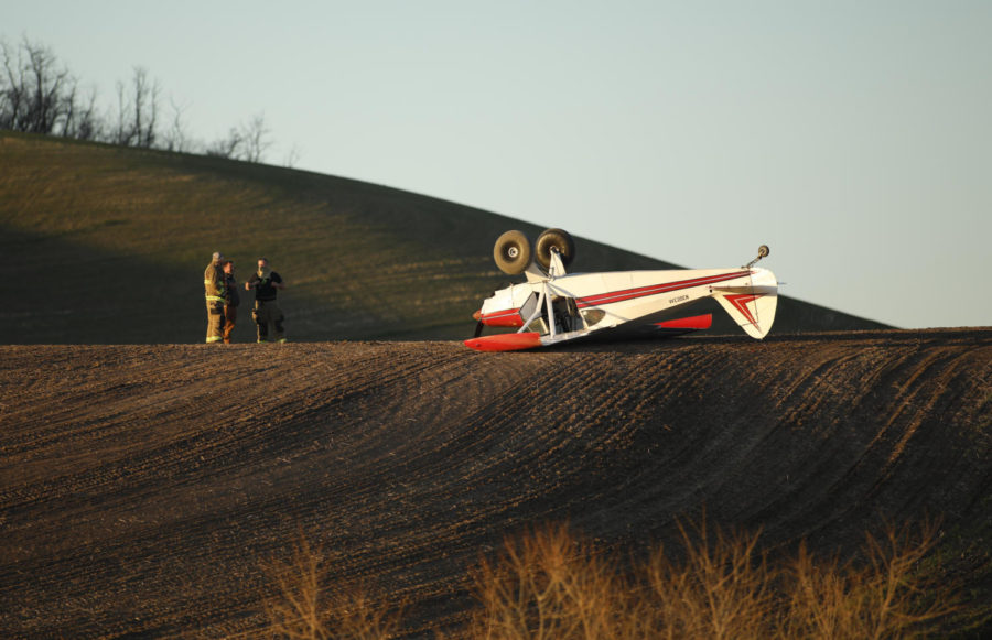 A small, single-person aircraft flipped over in a farmers field. 