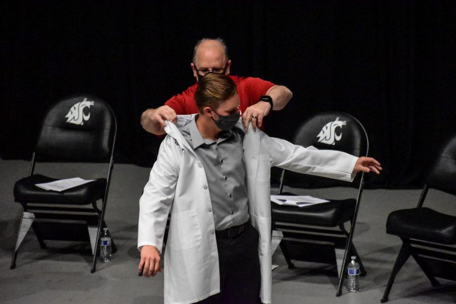 First-year veterinary student Jace Enwards receives his white coat from Dr. Rick DeBowes, Washington State Veterinary Medical Association president, at the ceremony Thursday afternoon in Beasley Coliseum.