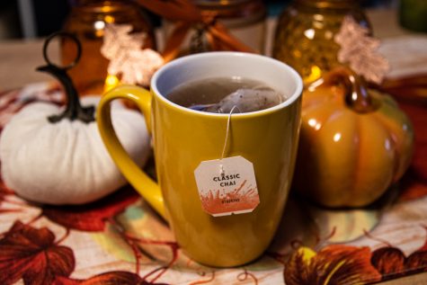 A hot cup of Chai tea in a yellow cup is surrounded by fall decor.
