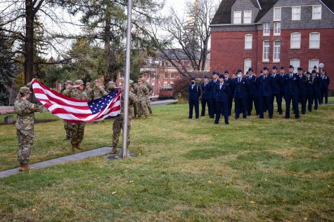 Army and Air Force ROTC cadets stand at attention and watch the American flag being hoisted up the flagpole.