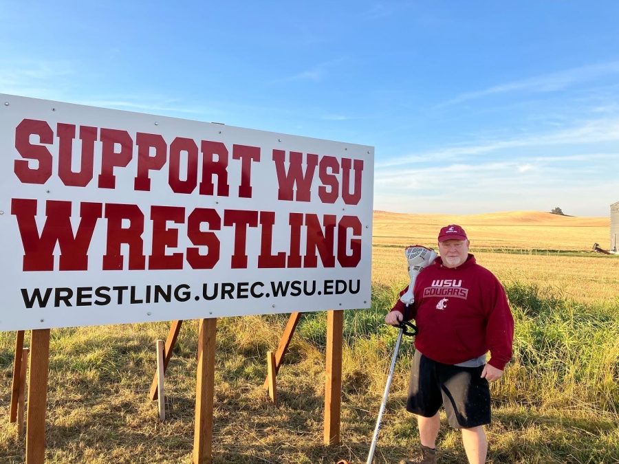 Phil+Burnett%2C+coach+of+WSU+wrestling+poses+next+to+the+support+WSU+wrestling+sign+along+Washington+Highway+26.