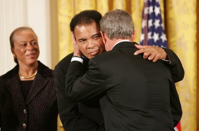 As Mrs. Lonnie Ali looks on, President George W. Bush embraces three-time heavyweight boxing champion of the world Muhammad Ali after presenting him with the Presidential Medal of Freedom Wednesday, Nov. 9, 2005, during ceremonies at the White House.