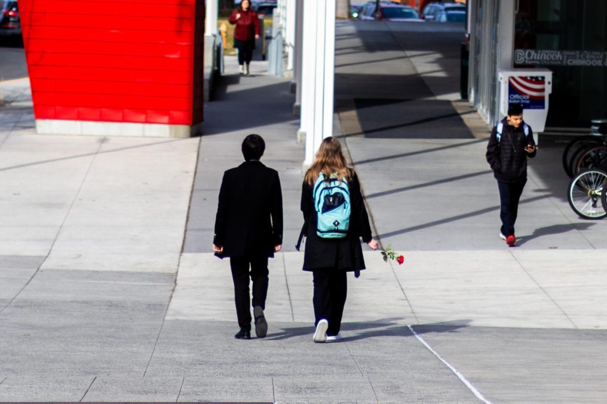 Two students walking on campus as one holds out a rose, Feb. 14, in Pullman, Wash. 
