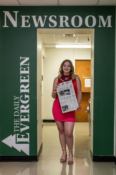 Anna Adams in front of The Daily Evergreen door in graduation regalia on April 20, 2024 in Pullman, Wash.
