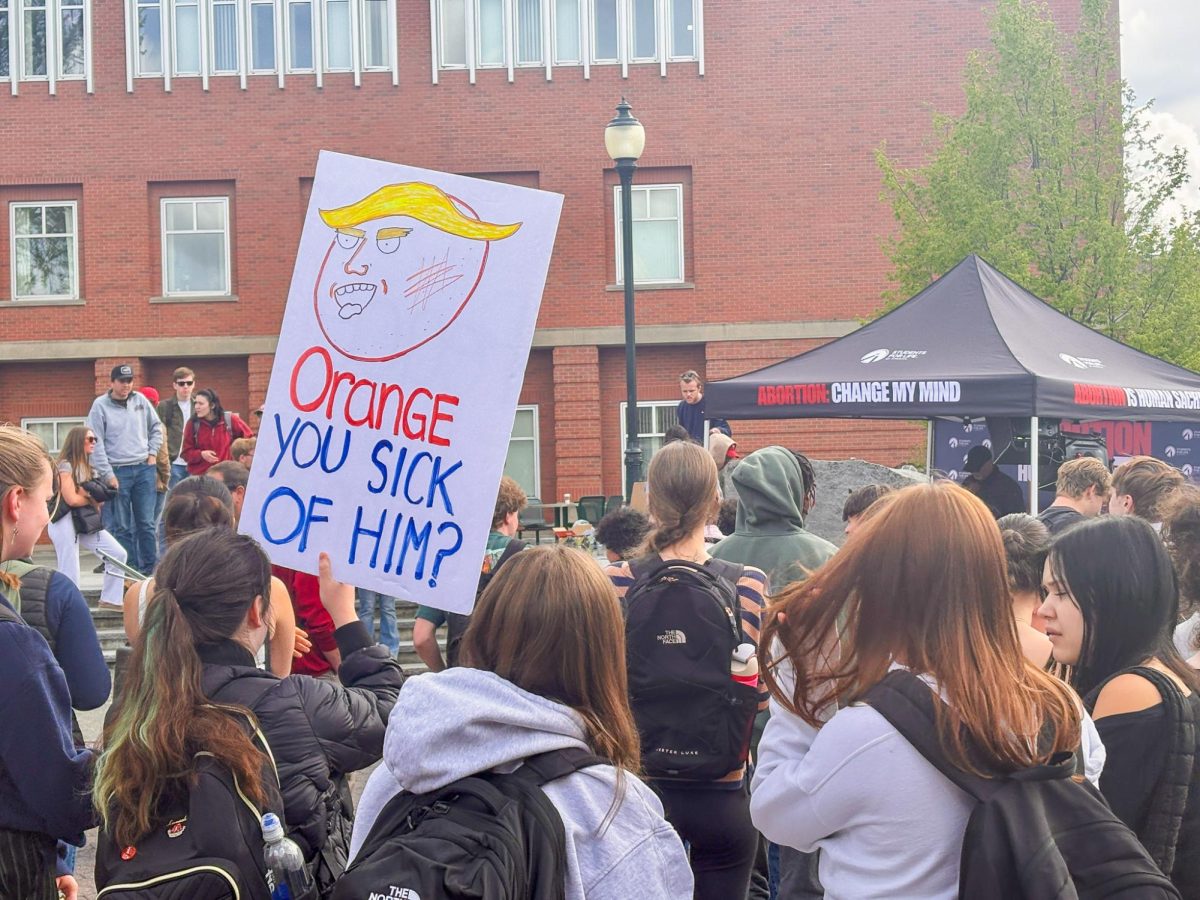 A student holding an anti-Trump sign in a group observing Turning Point USA's protest against abortion rights on Terrell Mall, April 28, 2026.